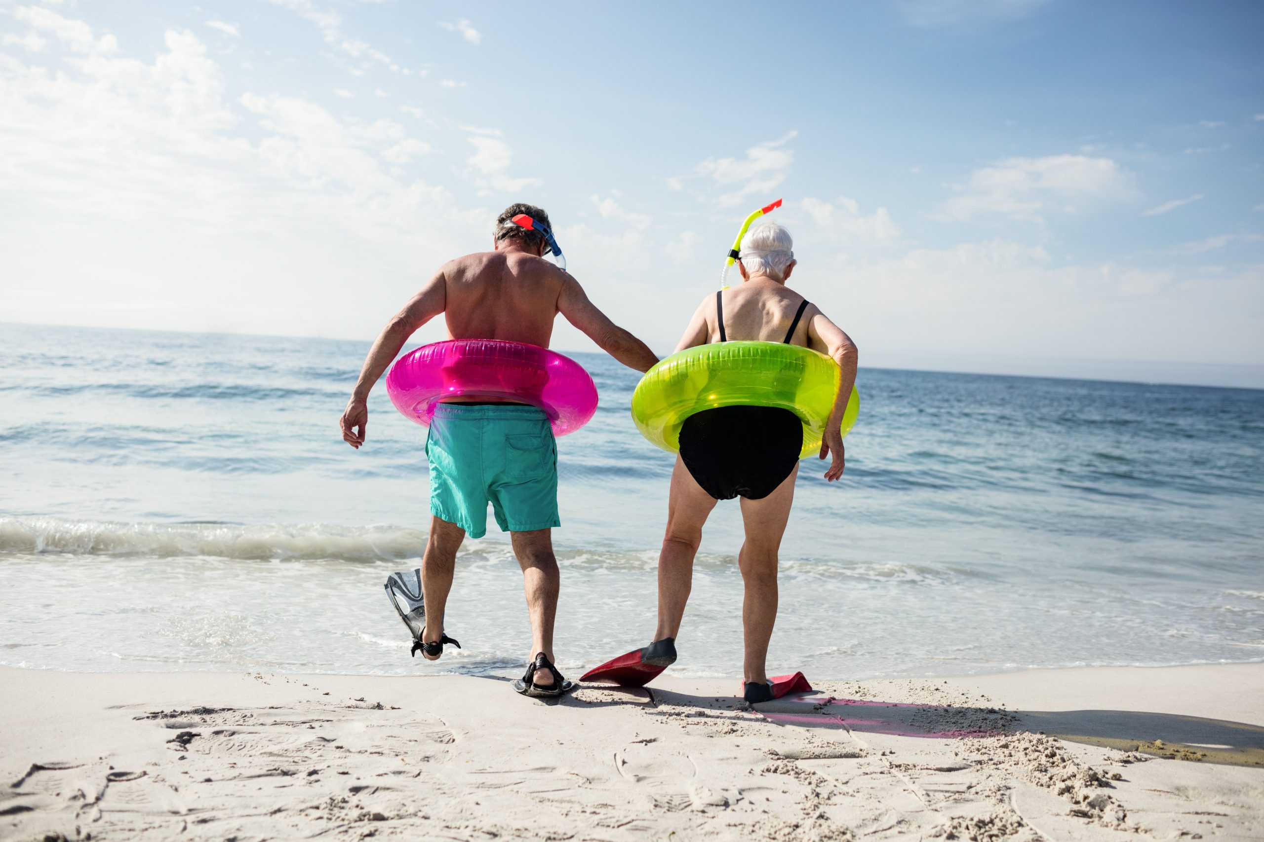 Senior couple in inflatable ring walking towards sea